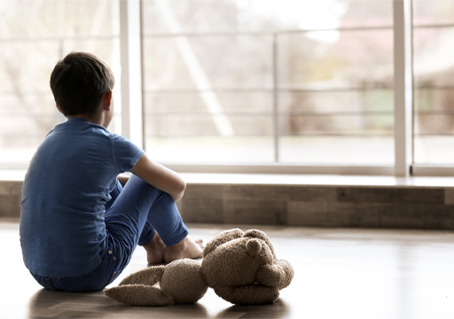 This is a photograph of a child with a teddy. They are sitting on the floor and looking out of a window.