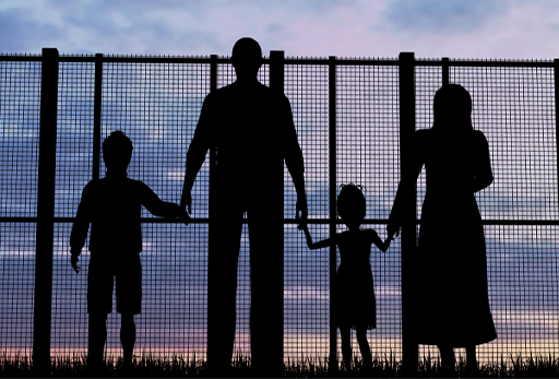 This is a photograph of a family in silhouette standing by a fence.