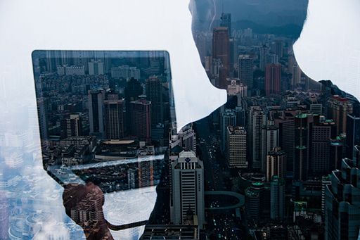 An abstract image of a cityscape with the shadow of a person holding a laptop over it.