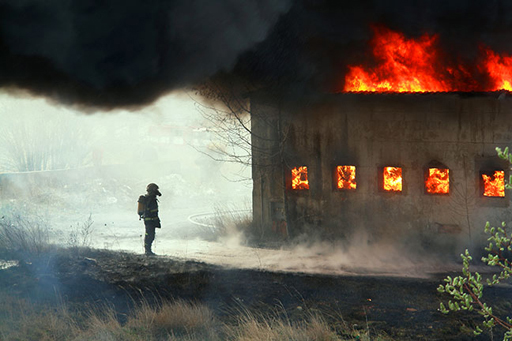 This is a photograph of a building on fire, with a firefighter looking on.