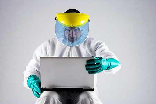 This photograph shows a man wearing protective clothing while using a laptop.
