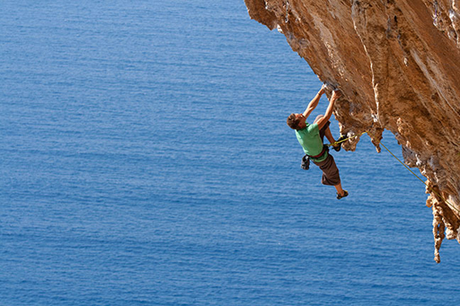 This is an image of a person climbing up a rock. The sea is in the background.