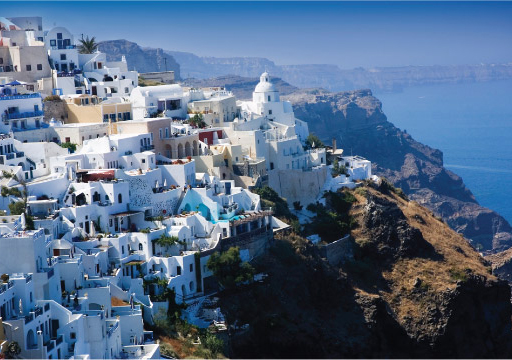 This photograph shows white houses on a hillside in Santorini, Greece.