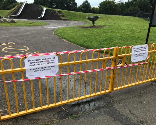 Photograph of yellow gates closing off a park with red tape over it and a sign stating that ‘due to recent vandalism the playground is closed for health and safety reasons. We hope to reopen the area as soon as possible.’