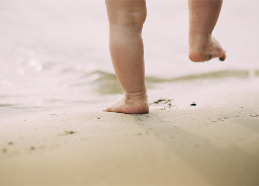 Photograph of a baby’s feet walking in the sand.