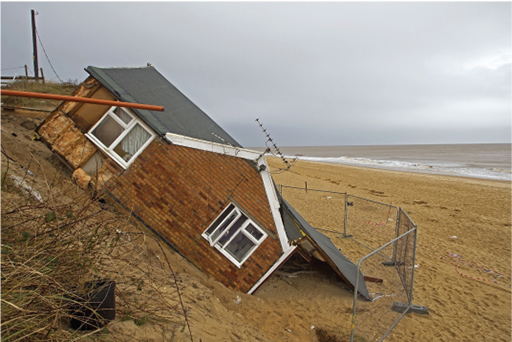 A photograph of a damaged chalet after coastal erosion caused by a tidal surge.