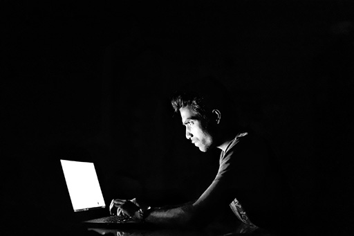 An image of a person in a dark room looking at a laptop.