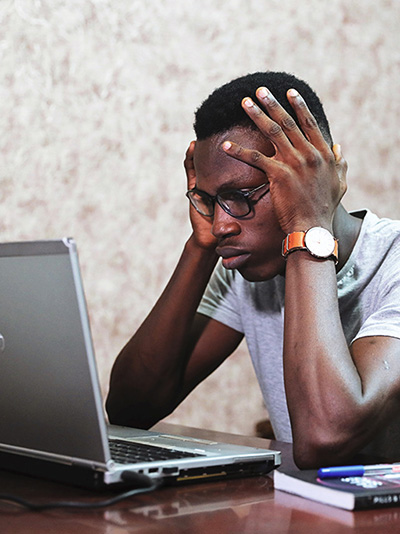 An image of a person with their head in their hands looking at a laptop.