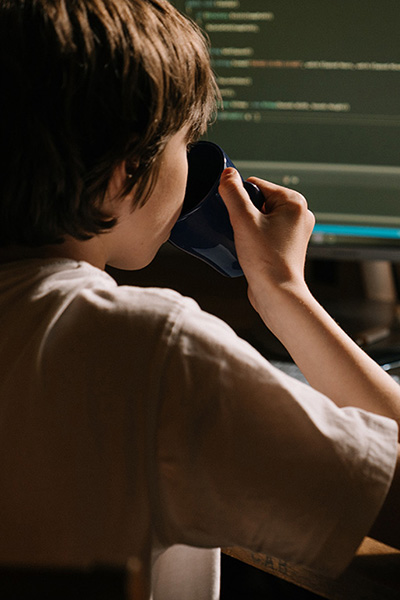 An image of a child drinking from a mug with a computer screen in the background.