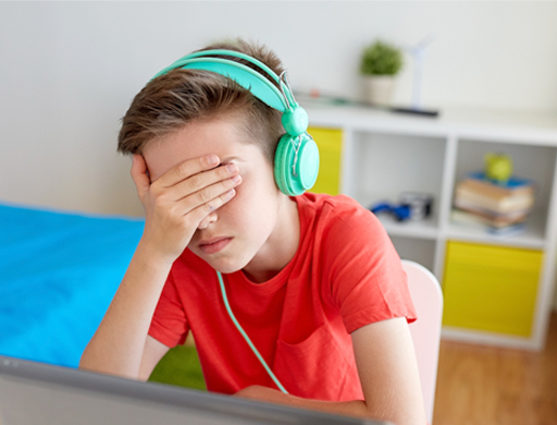 This is a photograph of a child wearing headphones, with their hand covering their face.