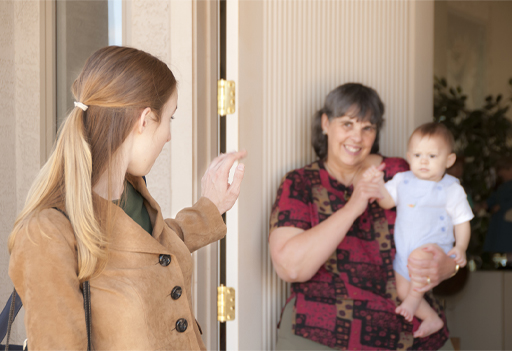 This is a photograph of a woman holding a baby while another woman waves and is walking away.