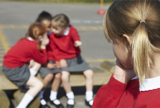 This is a photograph of a group of children sitting on a bench while another child looks on.