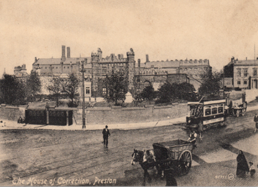 This is an early photograph of a substantial building in walled grounds, with an urban street in the foreground. A tram and a horse and cart approach from the right. The central part of the building has a castellated façade, featuring battlements flanked by two towers.