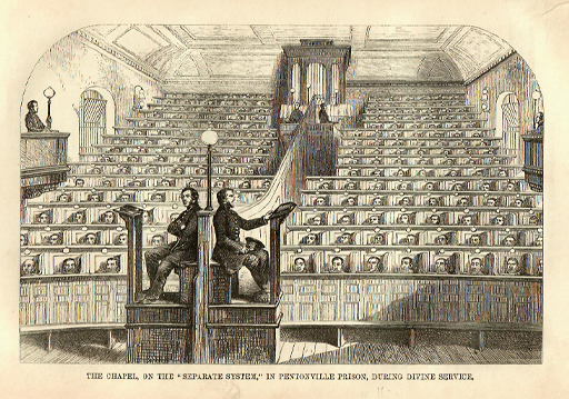 The tiered ranks of seating in this black and white drawing of a chapel rise and recede almost to ceiling height. They are filled with seated figures in partitioned cubicles. At the rear of the room is an organ, and two supervisors sit on raised podiums in the left foreground.