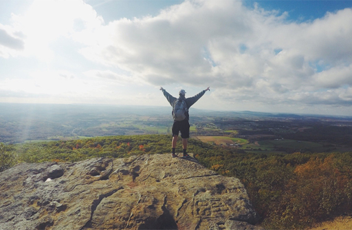 A person standing with their arms wide open on the top of a hill.