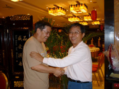 Two men shaking hands informally in a restaurant. One of the men has his hand on the other man’s arm too.