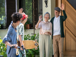 Photo of a man and woman aged 60–70 with two young boys, both waving goodbye to as the boys leave the grandparents house.
