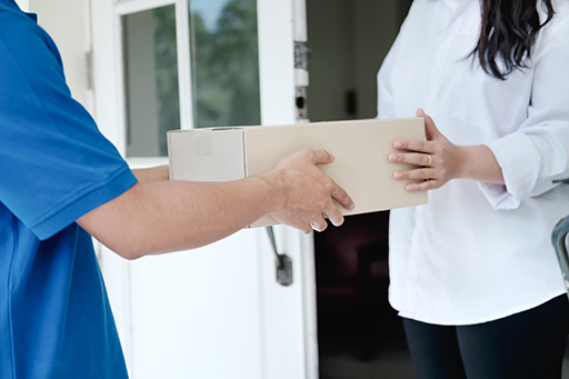 A woman standing in a doorway taking a parcel from a person in a blue t-shirt.