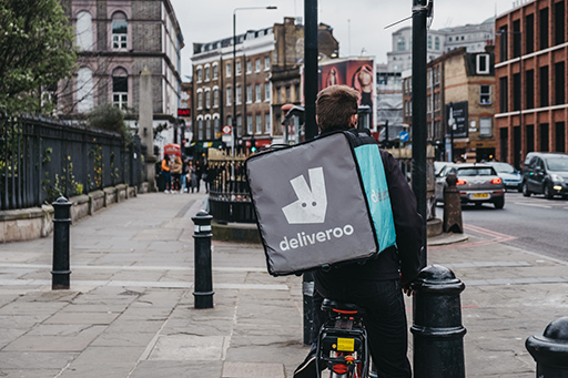 A deliveroo delivery person on their bike with a deliveroo bag on their back.