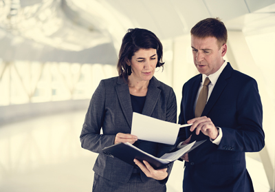 Two business people standing next to each other looking at a document in a file.