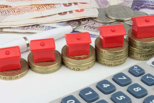 This shows a montage of bank notes and coins, a calculator and small plastic toy houses sitting on piles of coins.
