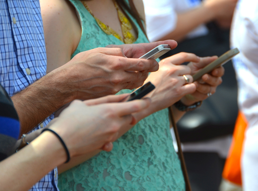 The figure is a photo showing three young people using their mobile phones.