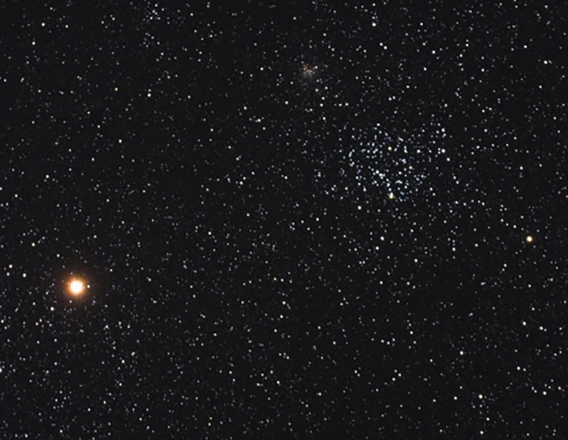 This is a photograph taken using a telescope of the nights sky. It shows Mars as a bright orange star, much larger than other smaller, white stars in the sky.