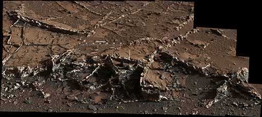 This figure is a photograph taken of a martian rock by the Curiosity rover. It covers approximately 180 cm from left to right. The rock is shades of dark brown, but there are criss-crossing white lines across its surface.