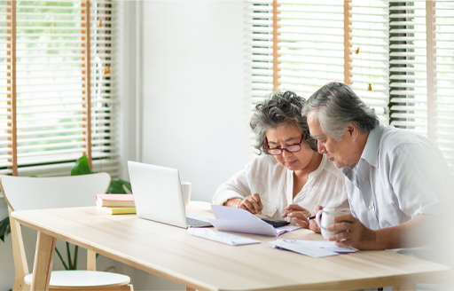 The figure shows a couple in their home poring over paperwork in front of their laptop.