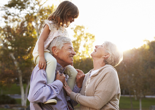 The figure is a photo showing a couple with their grandchild who is sitting on the shoulders of her grandfather.
