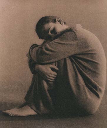Depressed or sad young person sitting on the floor with head resting on knees and arms wrapped around legs.