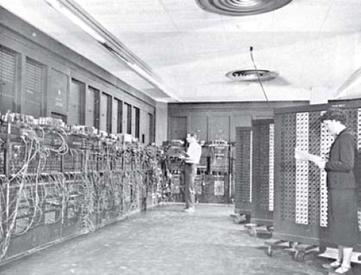 This is a black-and-white photograph of the ENIAC computer with two people standing next to it.
