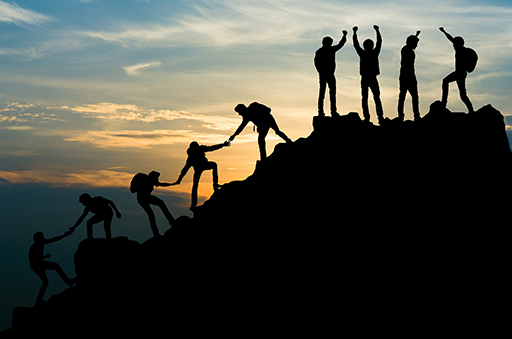 People helping each other by giving a hand to climb a rocky hill.