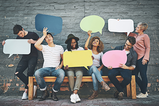 A group of six young individuals sat on a bench holding up blank speech bubbles.