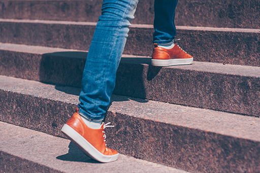 The legs of a person wearing jeans and trainers walking up steps.