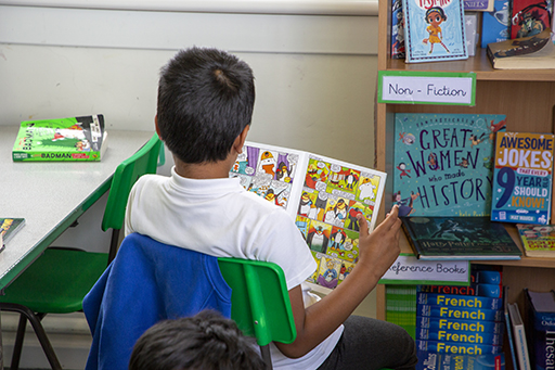 A school child with his back to the camera reading a graphic novel.
