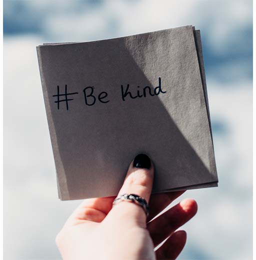 An image of a hand holding up a piece of paper that has the writing ‘#be kind’