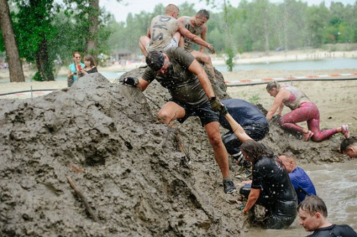 Image of men and women helping each other to climb over a mud barrier in a challenge race