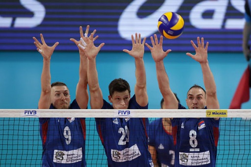 Image of three male volleyball players blocking a shot at the net