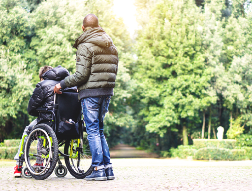Back view of a young carer with a young person with a disability on a wheelchair.