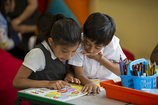 Two schoolchildren looking engrossed in a book together.