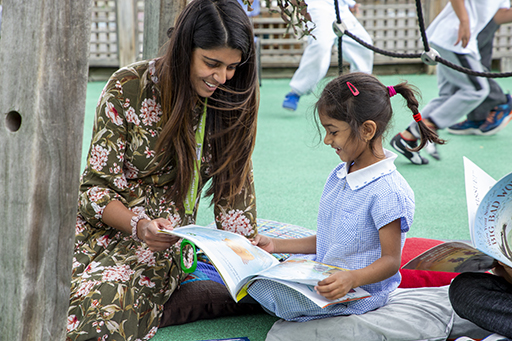 A teacher reading with a child outside on the playground.