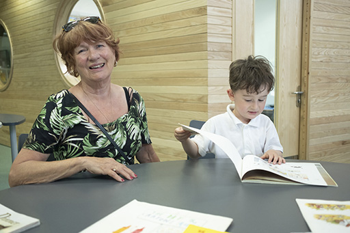 A reading volunteer sitting next to a young boy with a book.
