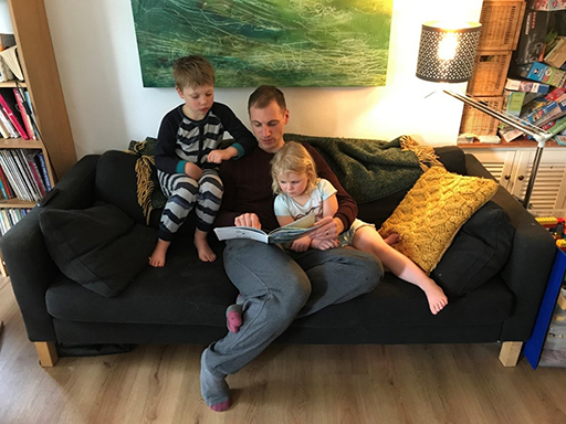 A parent reading on the sofa with his two children
