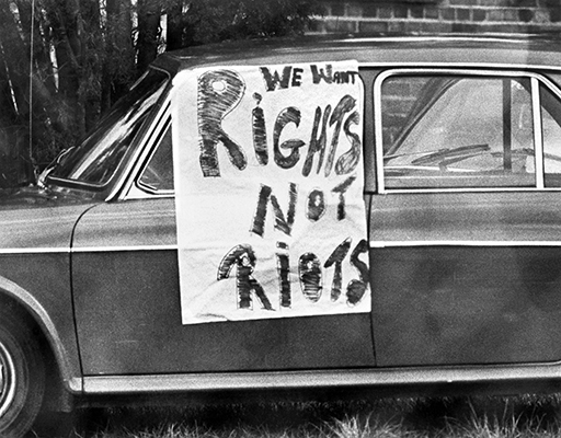 A photograph of a sign attached to a car which says ‘We want rights not riots’.