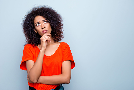 Woman standing with her hand on her chin looking puzzled.