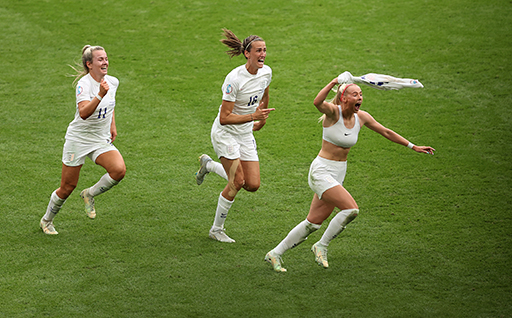 The figure shows three England footballers celebrating the winning goal of the 2022 Euros. The goal scorer has taken off her football shirt and it shows that she is wearing a sports bra.