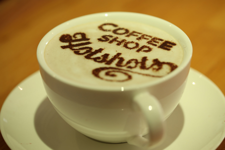 A cup of coffee with the words 'Coffee shop Hotshots' written in chocolate powder