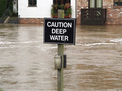 A sign displaying 'Caution Deep Water' stands in a flooded street