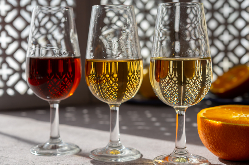 Glasses with cold dry fino and sweet cream sherry fortified wine and orange in sunlights, andalusian style interior 